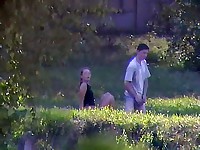 A clothed couple enjoying sex in the grass under spycam supervision